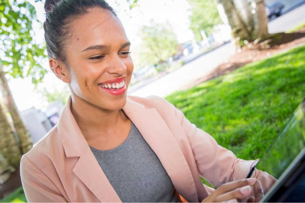 Smiling woman sitting outdoors and using a mobile device.