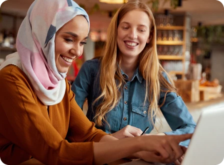 Two women in a coffee shop viewing online information on a laptop
