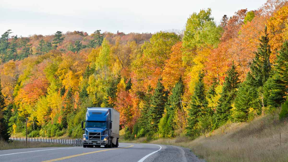 Photo of semi truck driving past autumn landscape