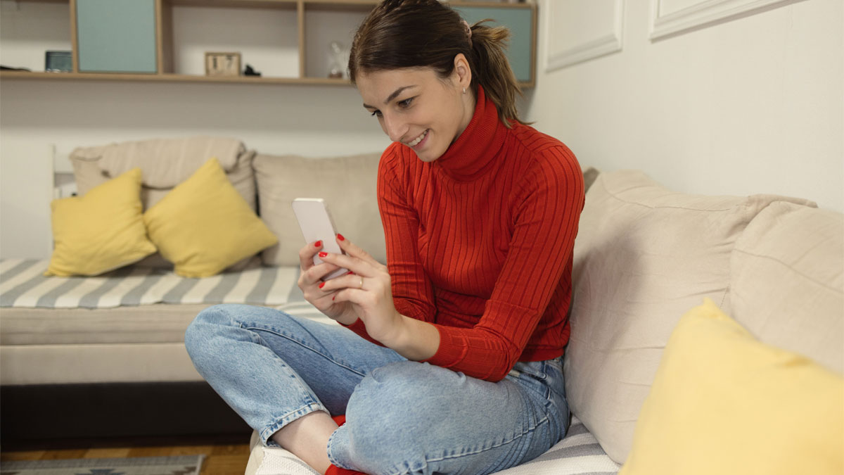 woman in red sweater sitting cross legged on coach looking at her phone