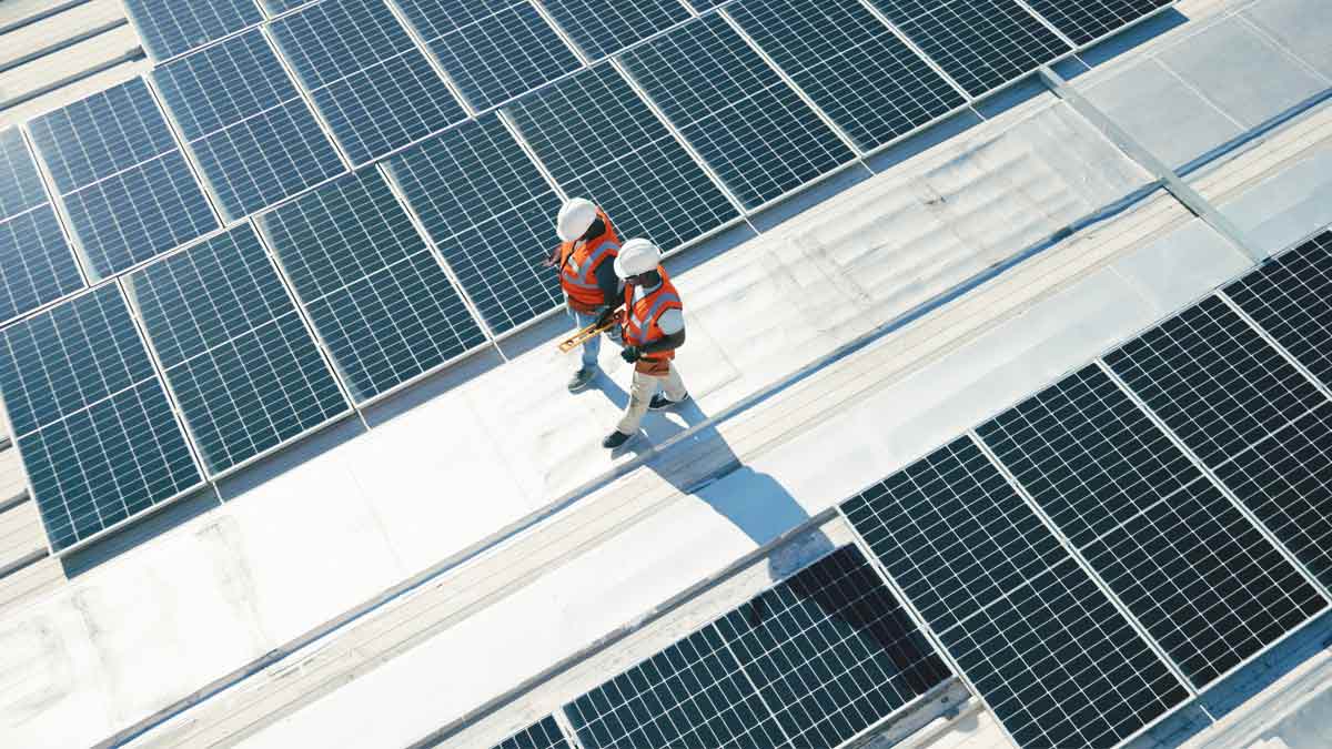 Two people in high visibility vests and hard hats walking through a field of solar panels, shot from above