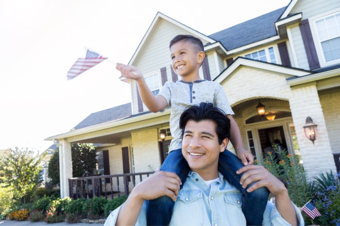 Young boy waving an American flag while sitting on his dad’s shoulders.