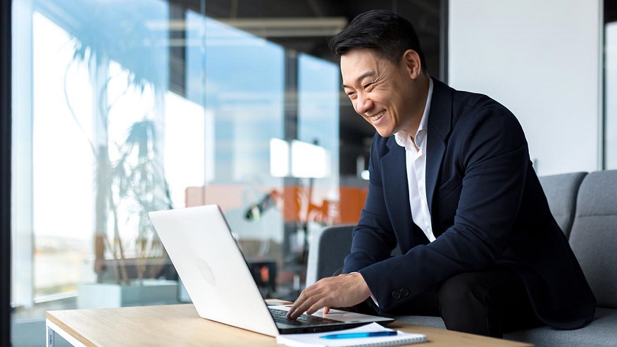 Smiling man in suit standing at his office desk looking at a computer