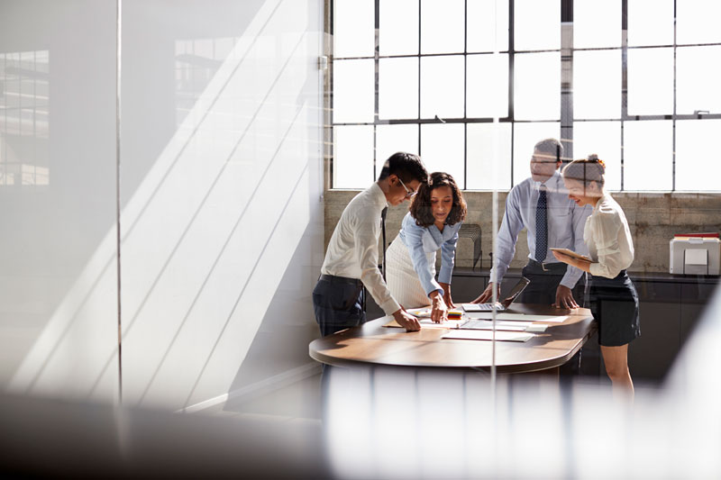 Four professionals standing around a table in a meeting room