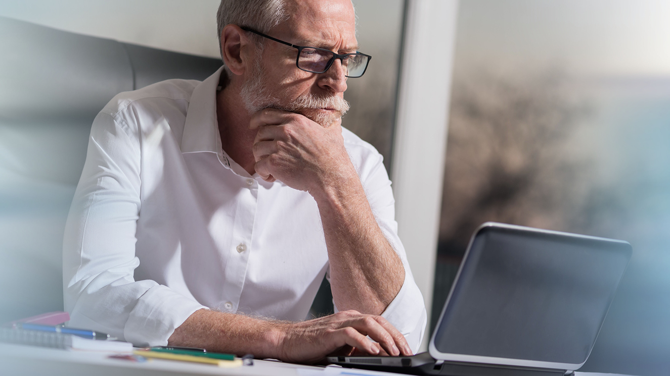 Man with glasses and a white beard with his hand on his chin as he browses the internet looking for help with ETFs.