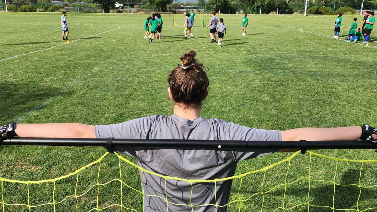 Photo of a soccer field with kids playing on it, taken from behind the goal