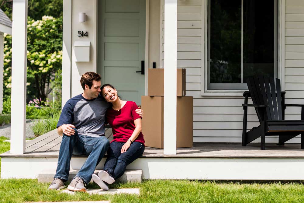 A man and woman sitting on the front porch of a home.