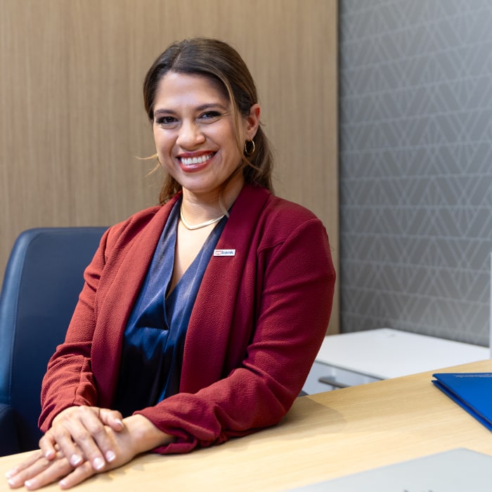 A young Hispanic woman with a U.S. Bank badge sits at a desk, smiling for the camera.