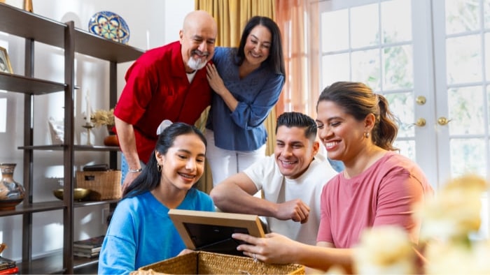 Tres generaciones de una familia hispana sentados en su sala viendo fotografías familiares.