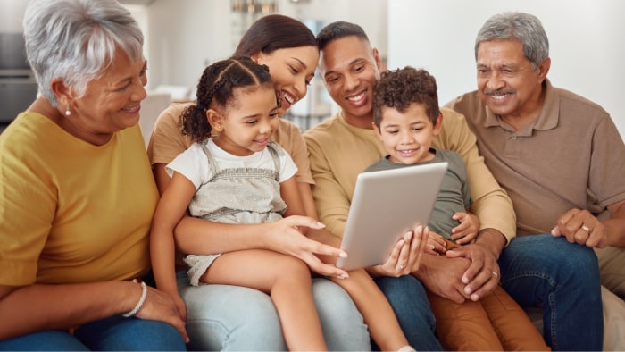 A multigenerational family is in their living room looking at the same tablet.